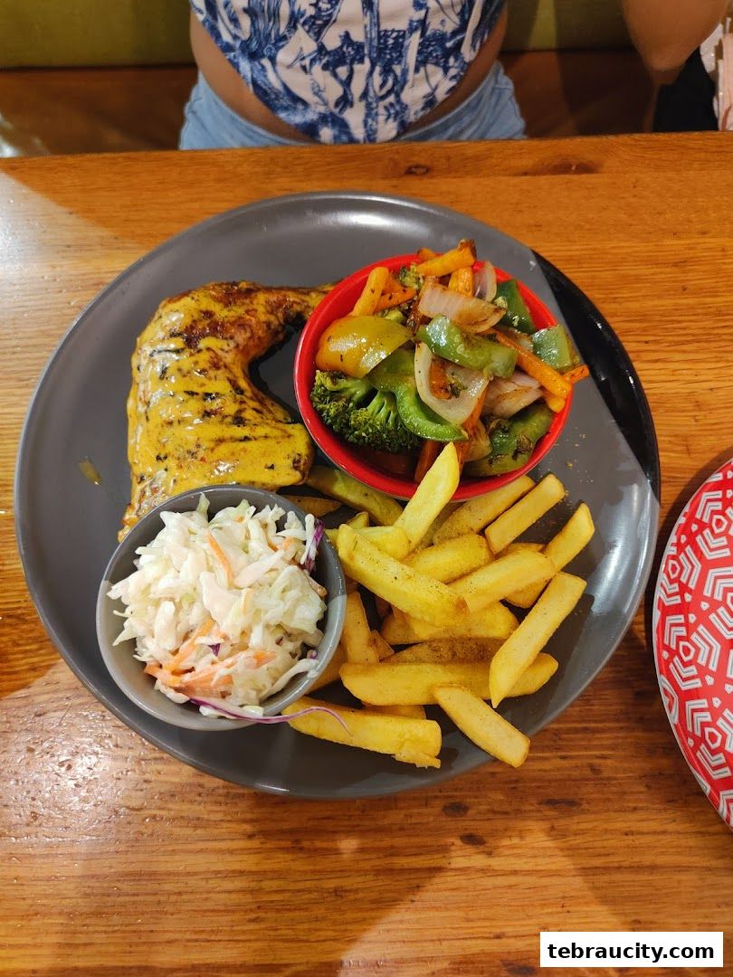 A plate of grilled chicken with fries, coleslaw, and mixed vegetables.