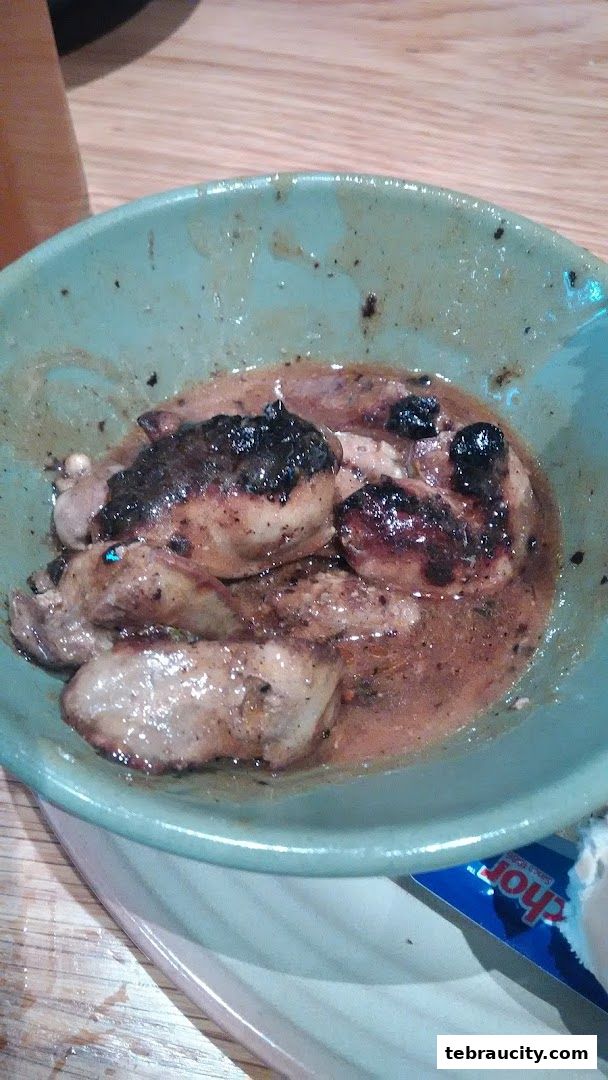 A close-up of peri-peri chicken pieces in a light brown sauce in a teal bowl.