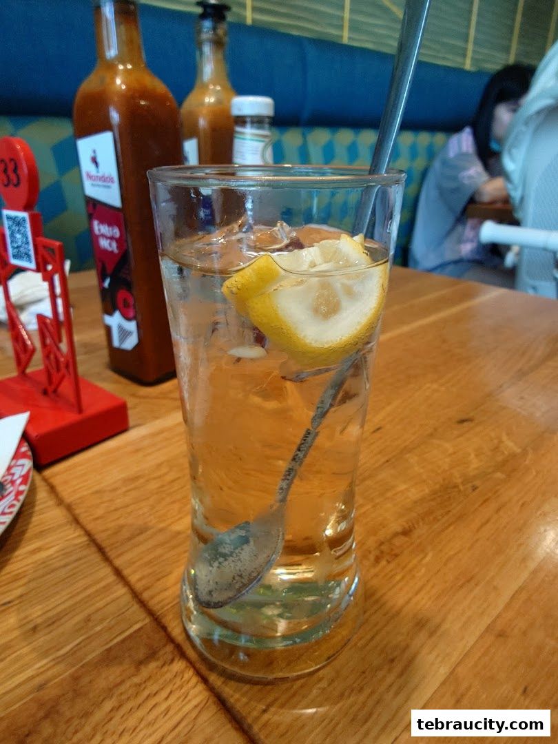 A glass of iced water with lemon and a spoon on a wooden table at Nando's.