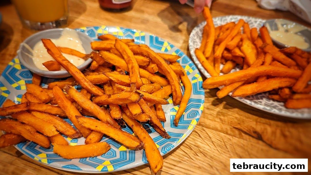 Two plates of crispy sweet potato fries with dipping sauce on a wooden table.
