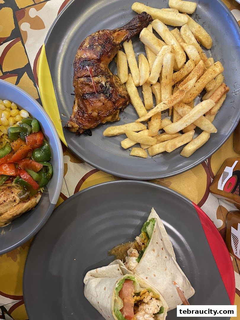 Plates of grilled chicken with fries and wraps, alongside a bowl of corn and peppers.