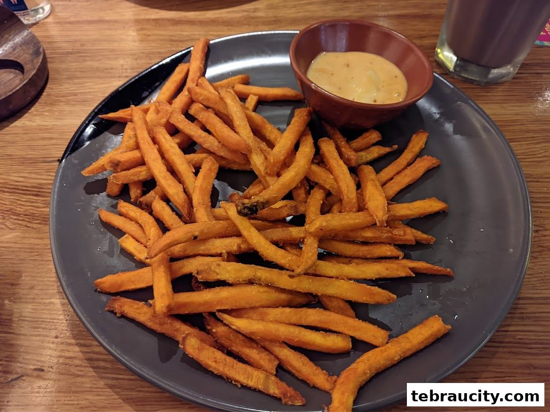 A plate of sweet potato fries with a side of dipping sauce on a wooden table.