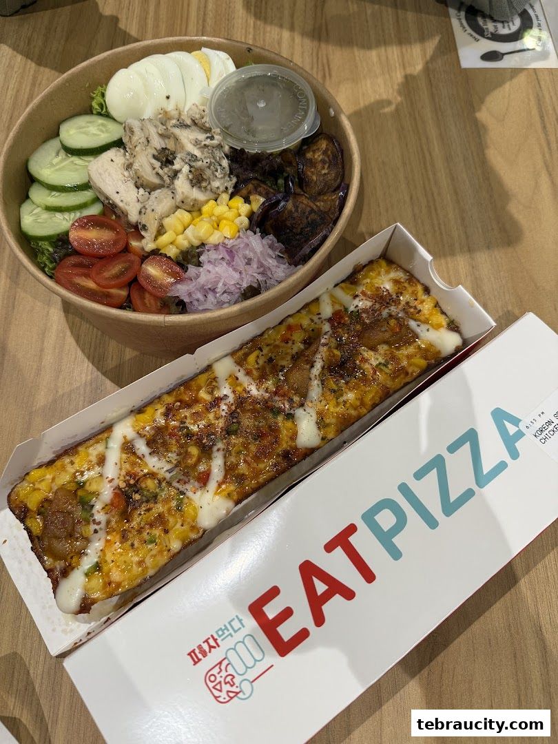 A delicious salad bowl and a long pizza slice with Korean style chicken.
