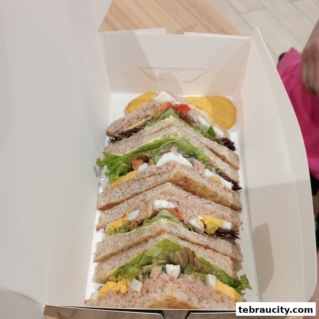 A box filled with freshly made sandwiches, cut into triangles, with chips on the side.