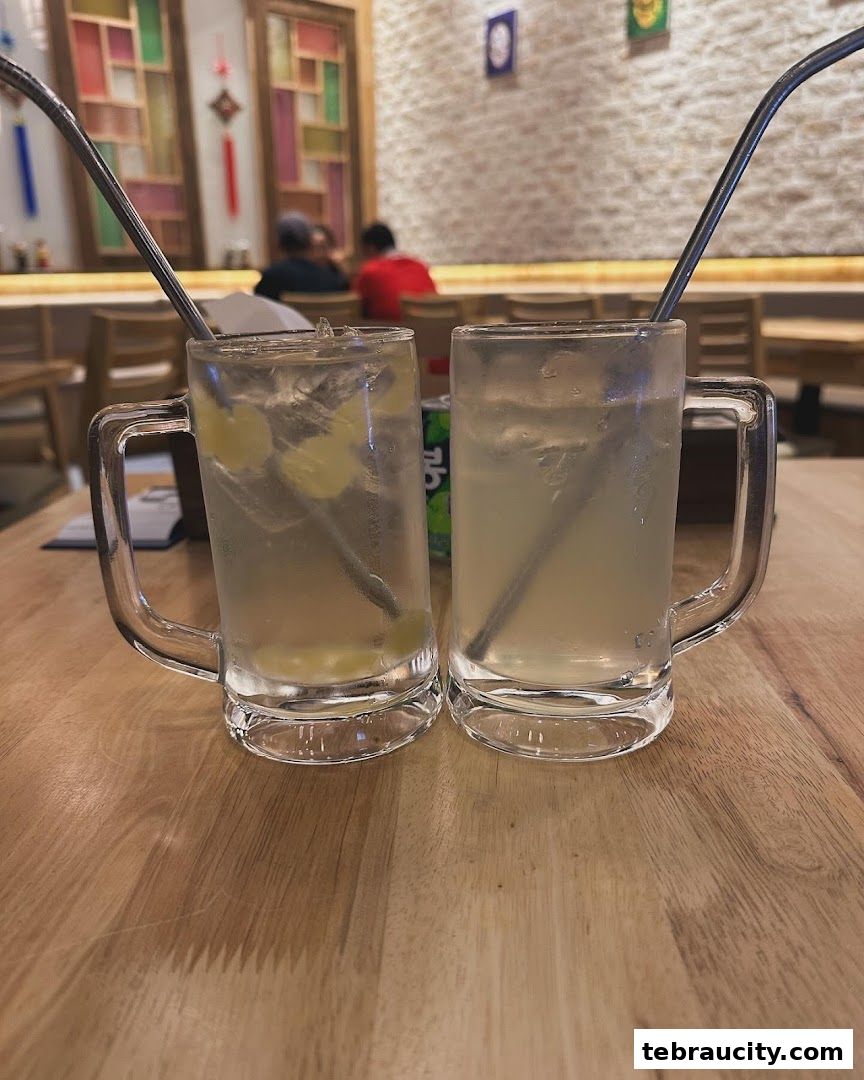Two refreshing drinks with metal straws on a wooden table at Oiso Korean Restaurant.