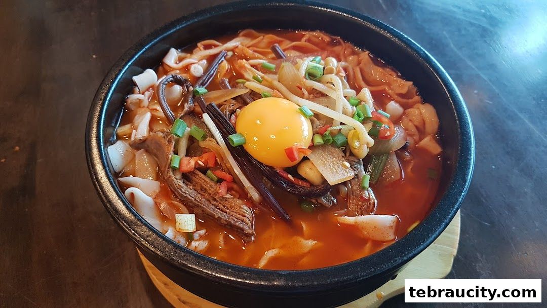 A close-up of a steaming bowl of Korean noodle soup with a raw egg yolk.