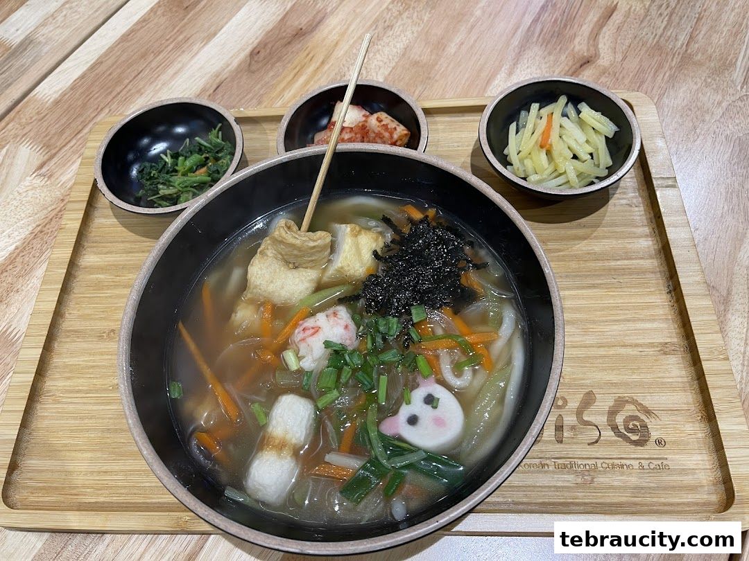 A steaming bowl of Korean noodle soup with various toppings and side dishes.