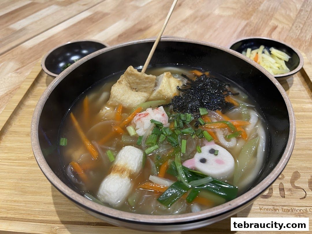 A delicious bowl of Korean udon soup with various toppings and a side of pickled radish.