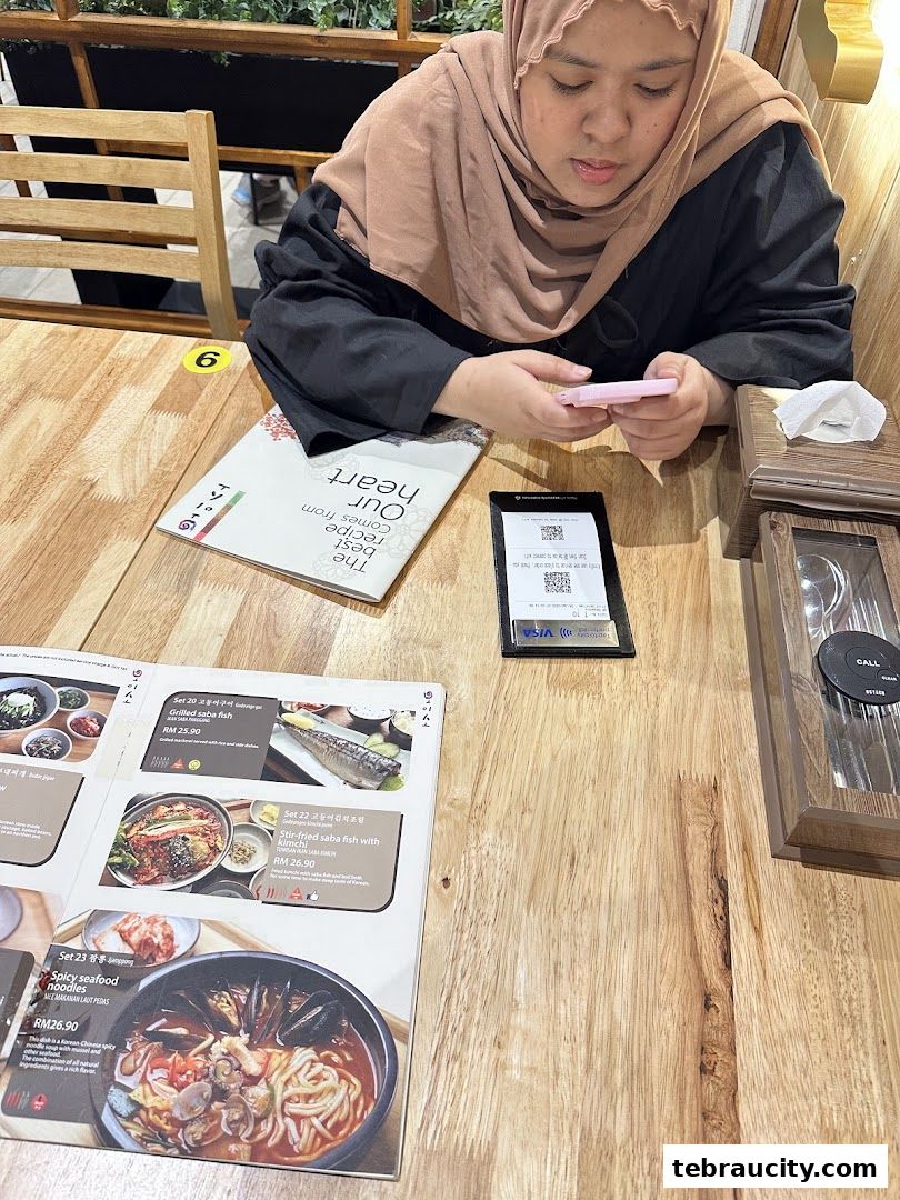 A person looking at a menu at Oiso Korean Restaurant with various Korean dishes displayed.