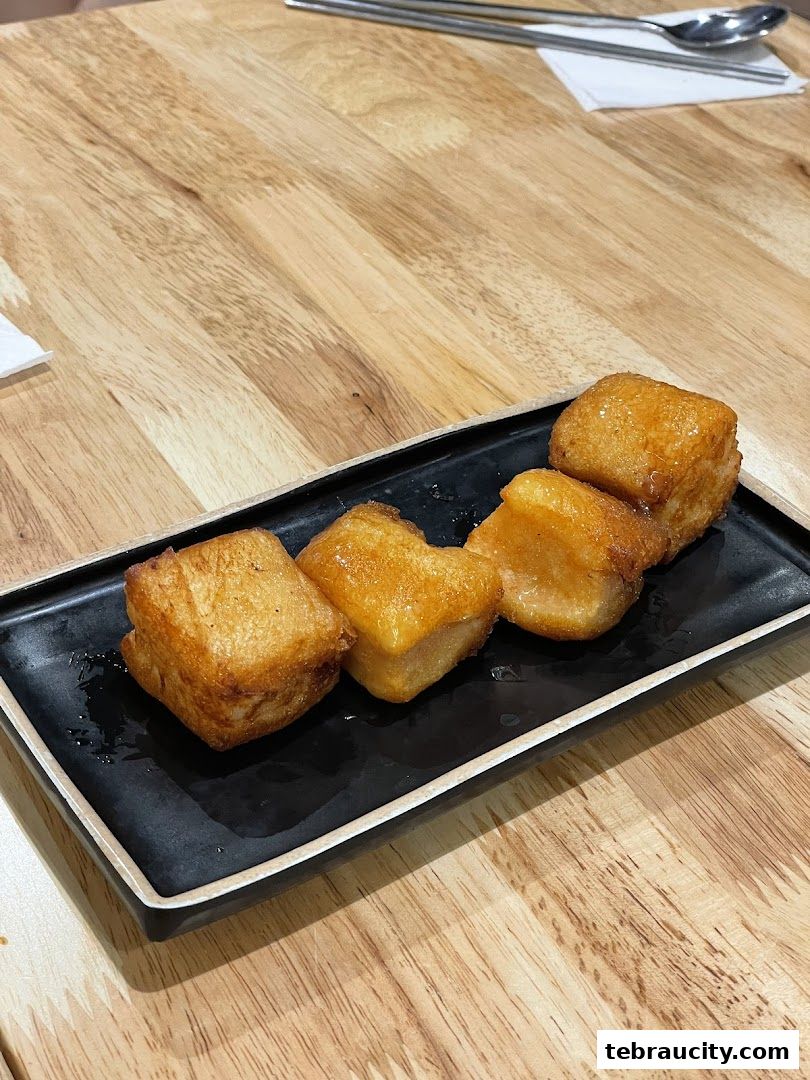 Golden fried Korean rice cakes served on a black rectangular plate on a wooden table.