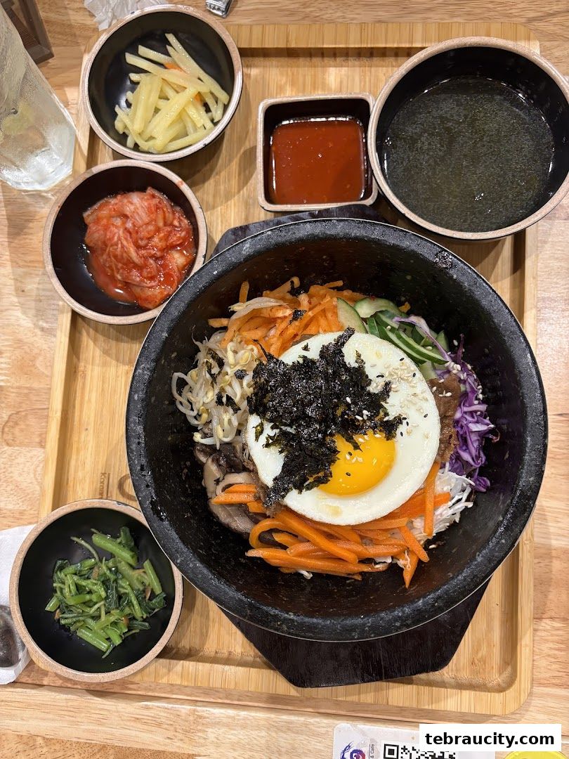 A delicious Korean bibimbap served in a hot stone bowl with side dishes and soup.