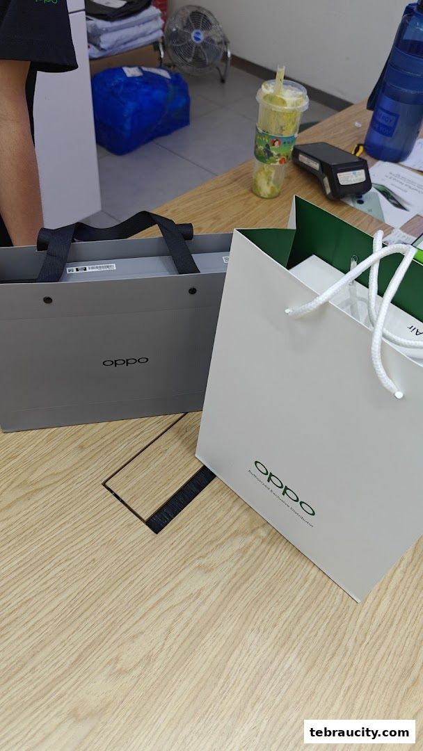 Two OPPO branded shopping bags on a wooden counter with a drink and payment terminal.