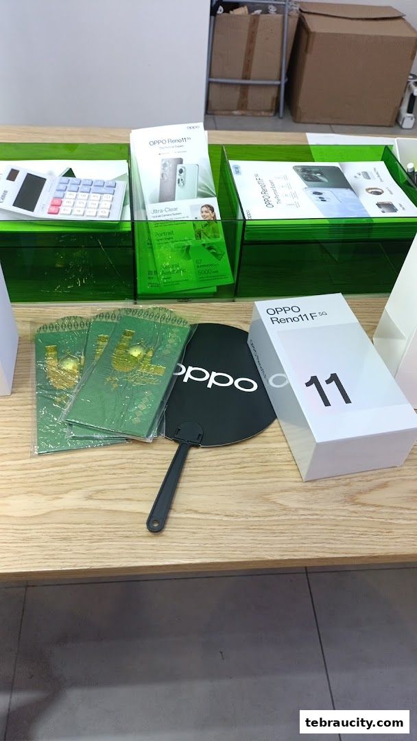 OPPO Reno11 F 5G phone box, promotional materials, and a branded fan on a wooden counter.