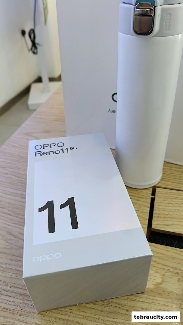 A box for the OPPO Reno11 5G smartphone and a white thermos on a wooden surface.
