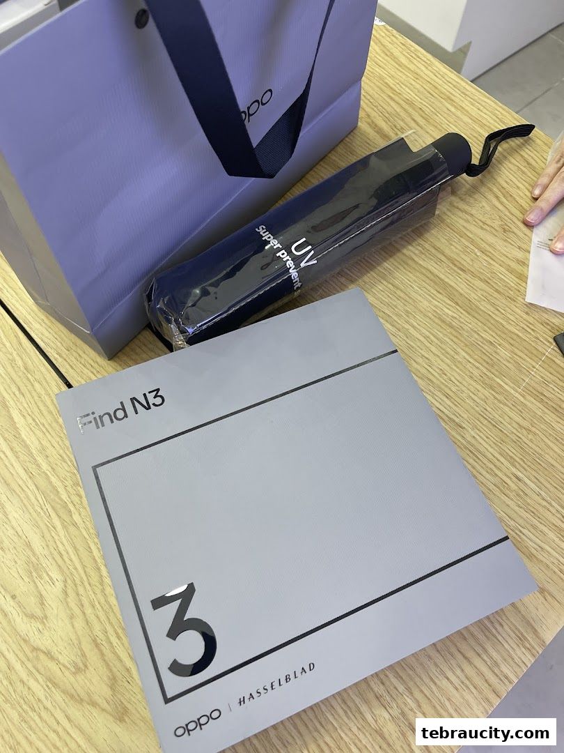 OPPO Find N3 box, shopping bag, and a UV umbrella on a wooden surface.