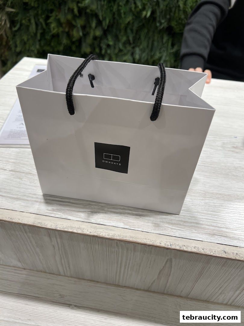 A white shopping bag with the OWNDAYS logo on a wooden counter.