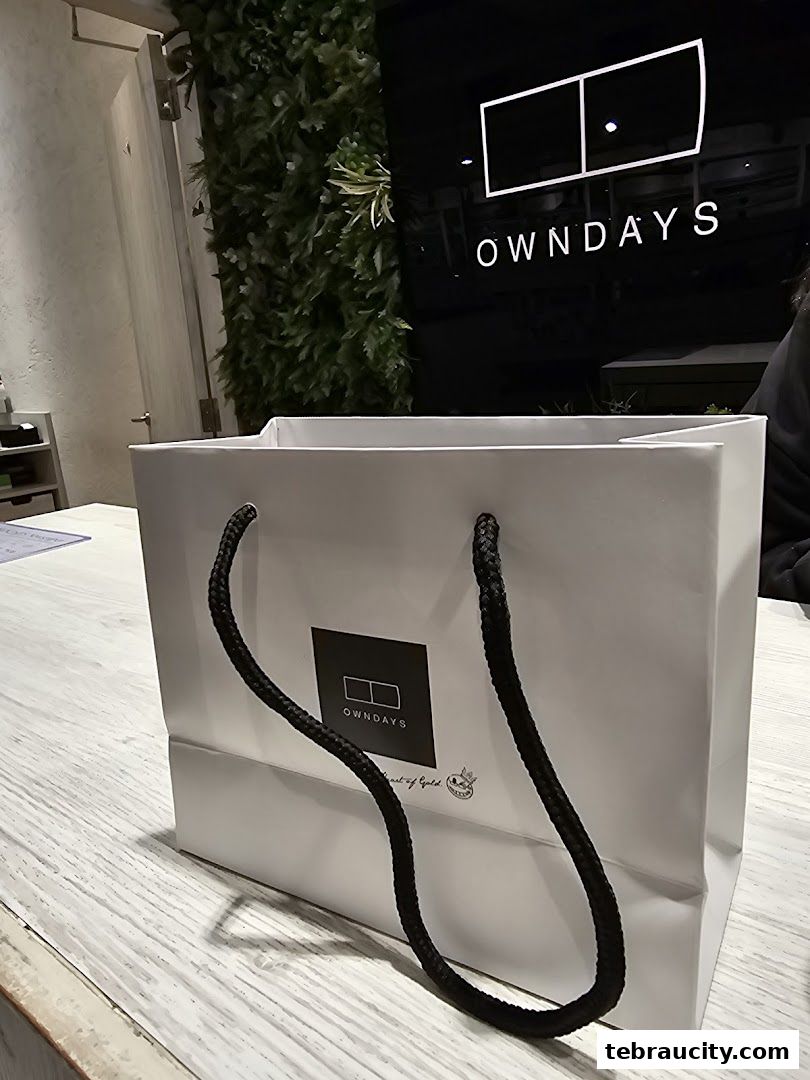 A white shopping bag with the OWNDAYS logo sits on a wooden table.