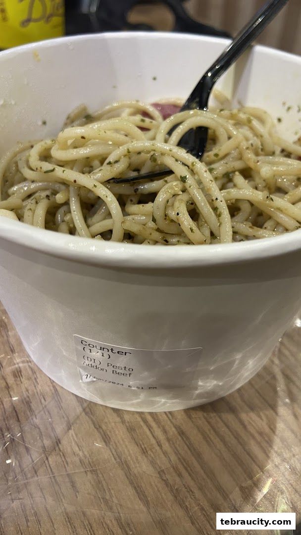 A close-up of a bowl of spaghetti with pesto sauce and beef, with a fork inside.