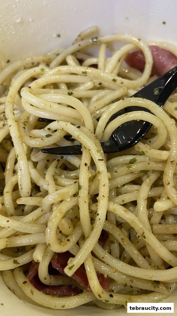 A close-up shot of a bowl of spaghetti with a fork, featuring a light sauce and visible herbs.
