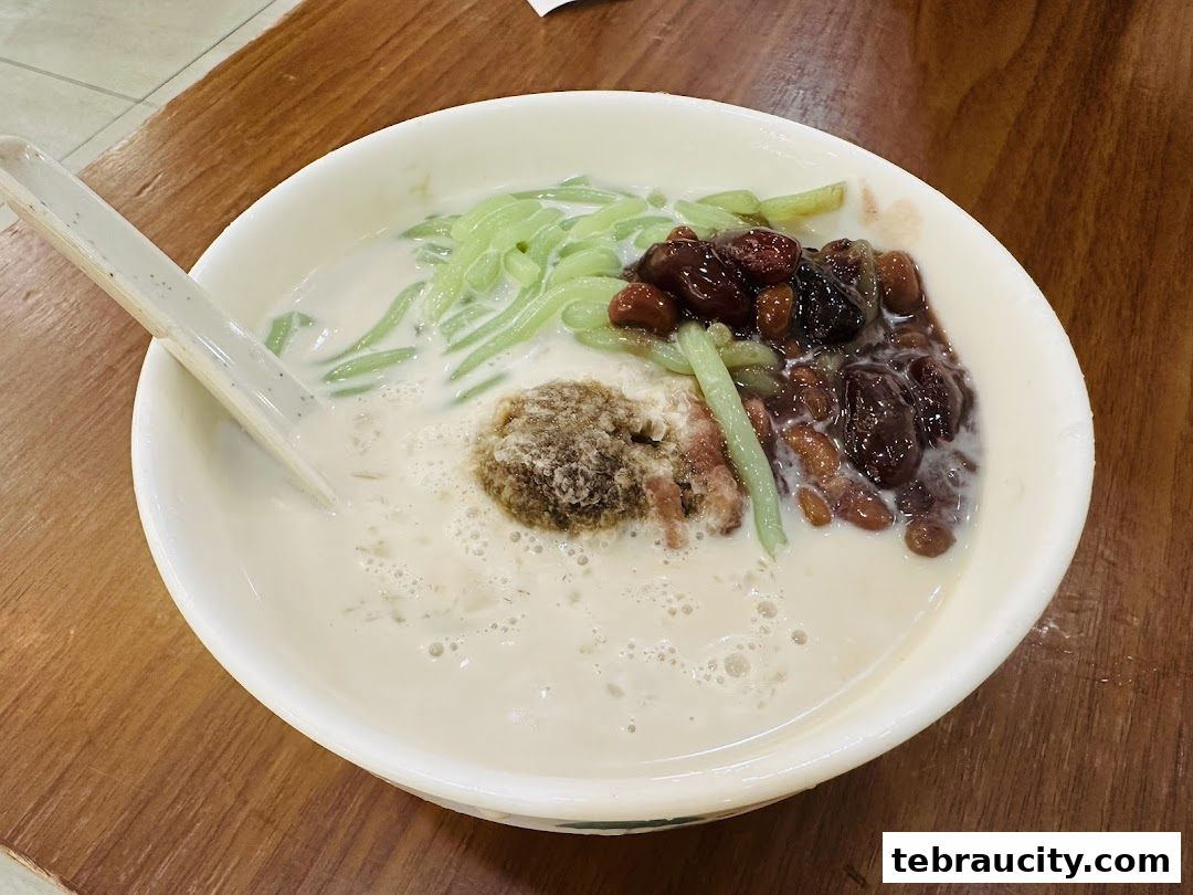 A bowl of Chendol dessert with green jelly, red beans, and shaved ice in coconut milk.