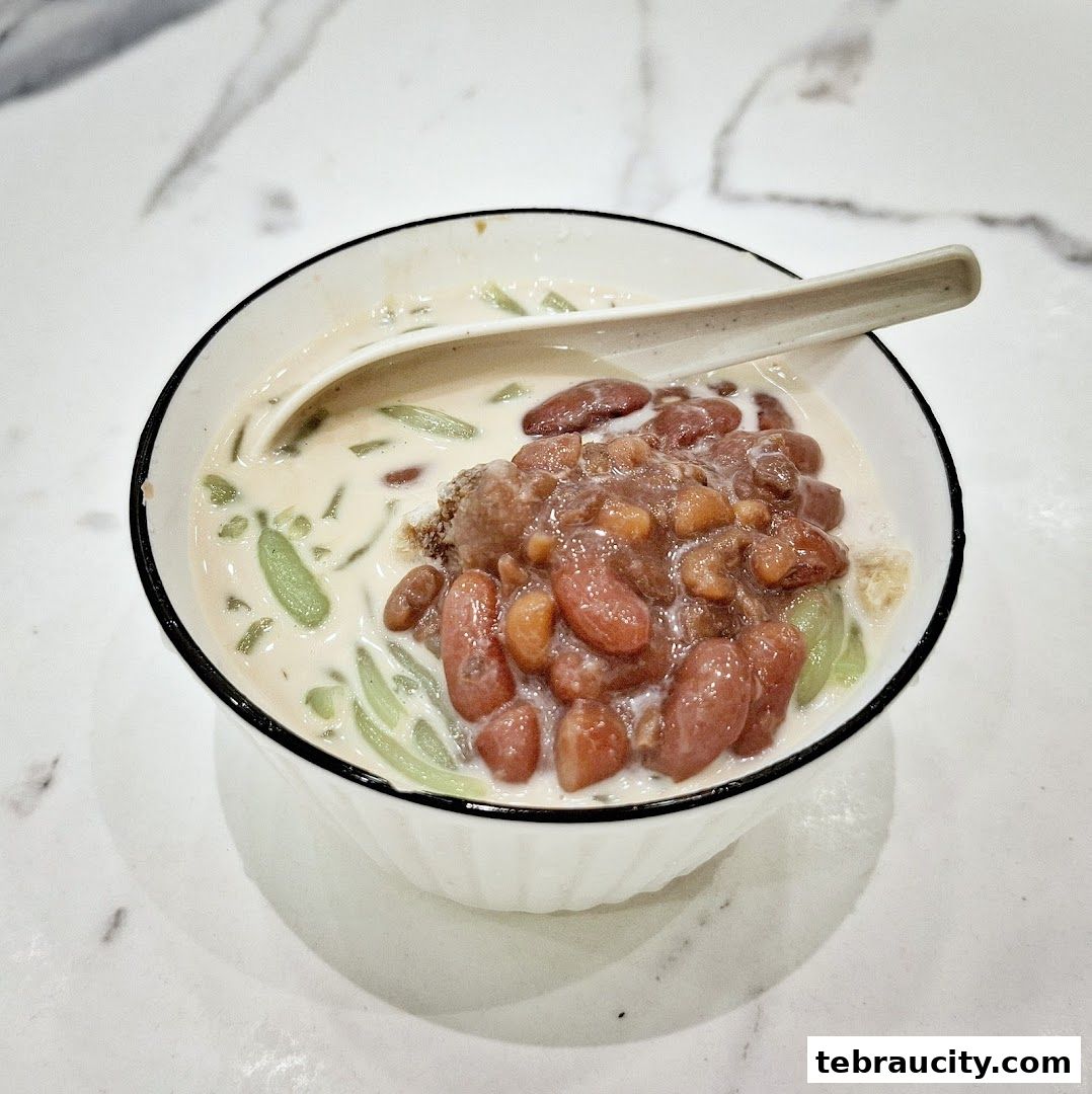 A close-up shot of a bowl of Chendol dessert with red beans and shaved ice.