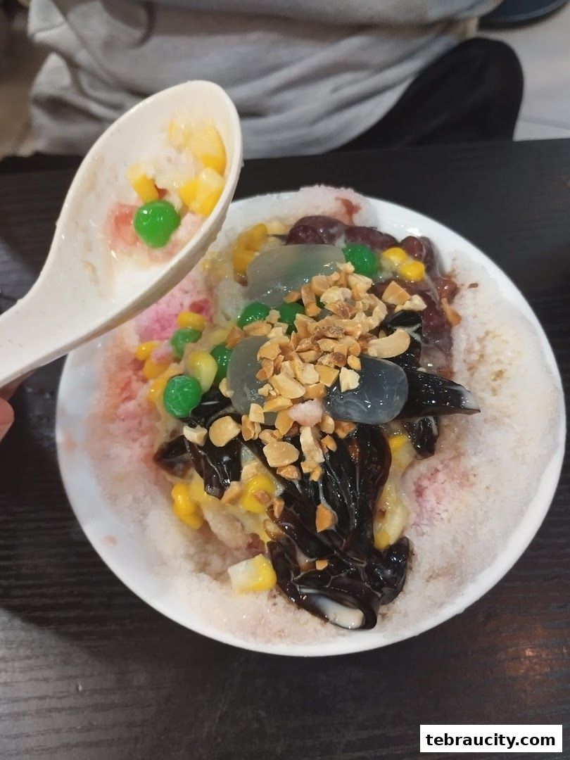 A close-up of a bowl of shaved ice dessert with various toppings, including corn, beans, and jelly.