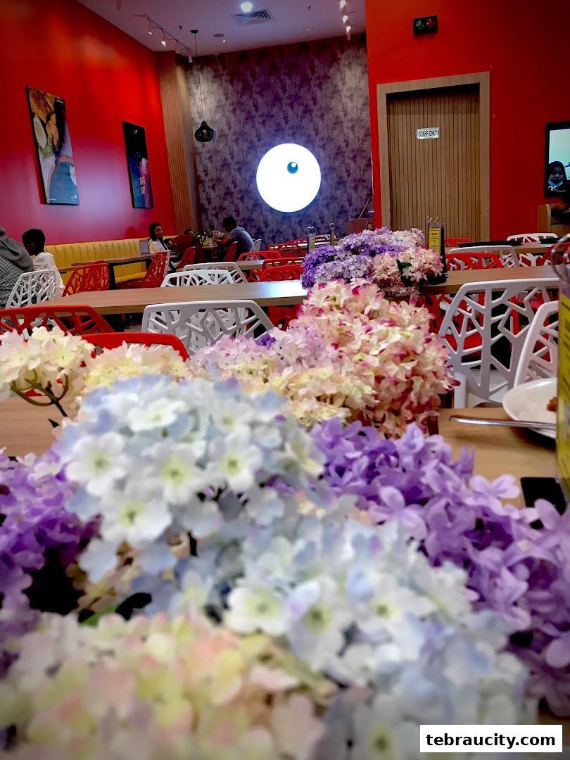Interior of a restaurant with colorful flowers on tables and red walls.