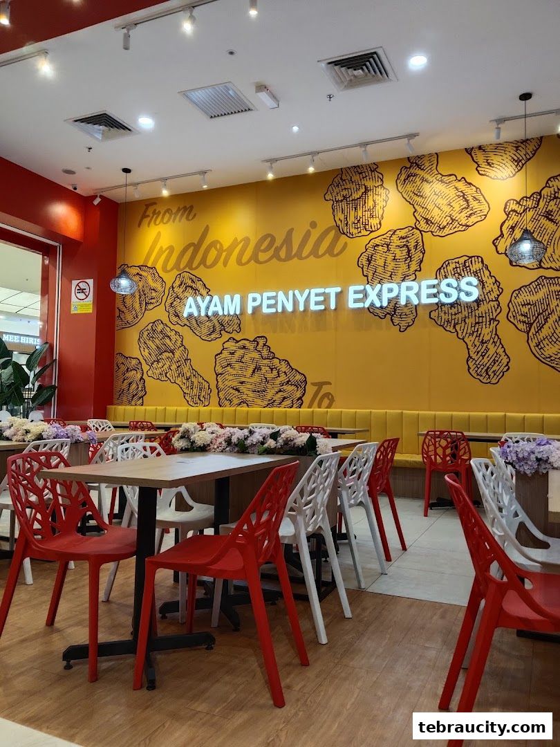 Interior of Ayam Penyet Express with yellow walls, neon sign, and red and white chairs.