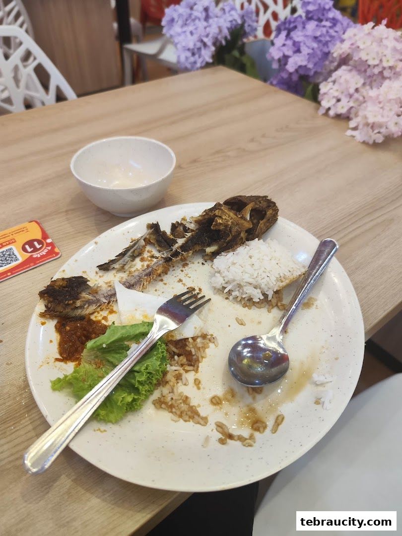 A plate with leftover food, rice, and a fork and spoon on a wooden table.