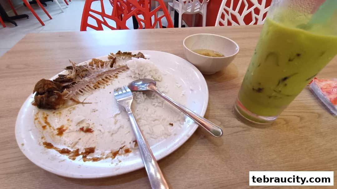 A plate with leftover fish bones, rice, and a glass of green drink on a wooden table.
