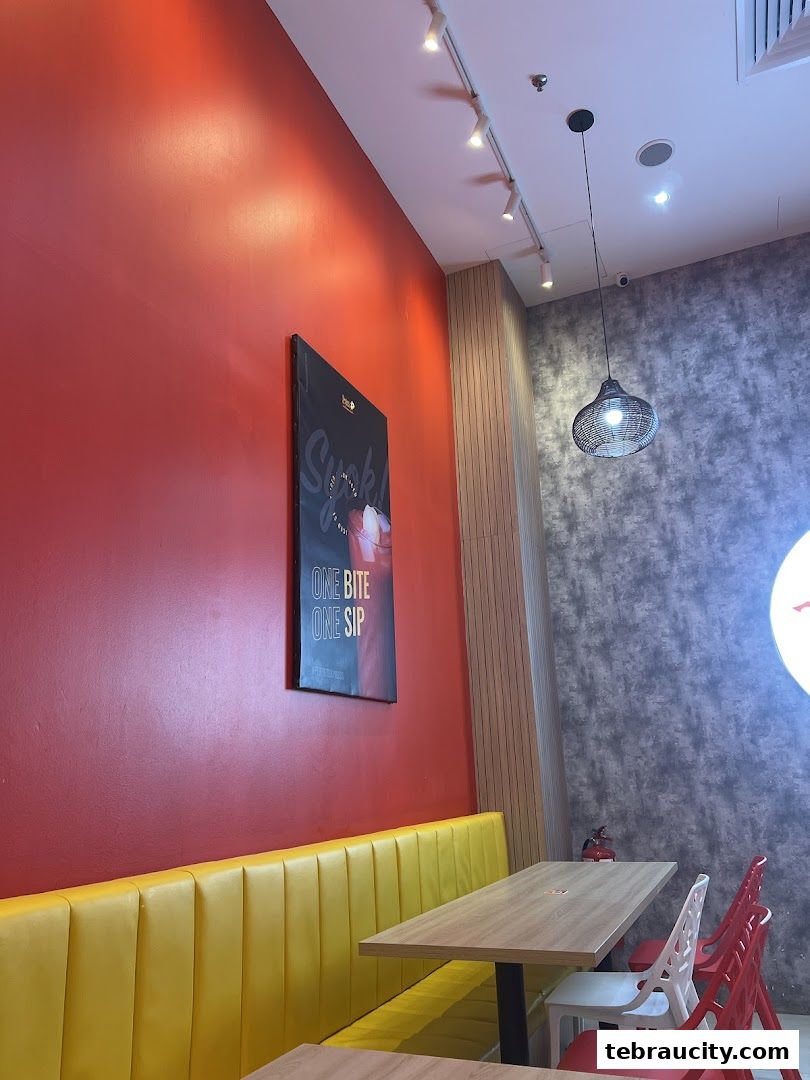 Interior of a restaurant with red and grey walls, yellow banquette seating, and tables with chairs.