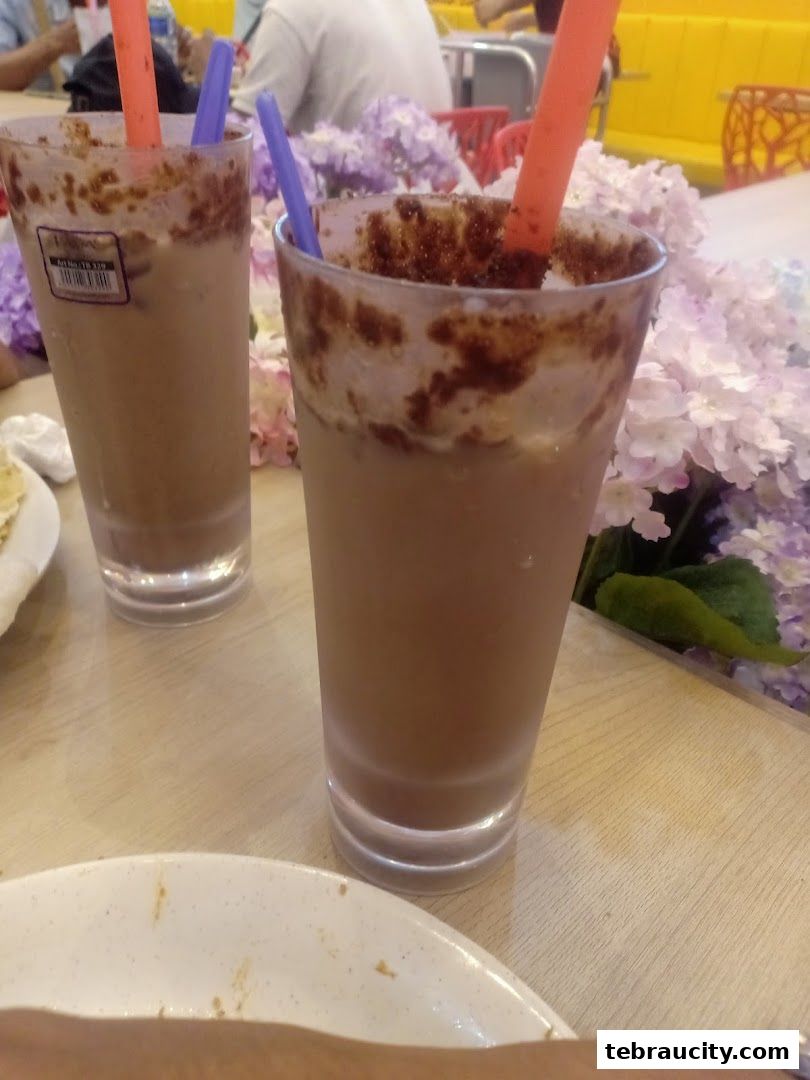 Two iced chocolate drinks with straws and chocolate drizzle on the rim, placed on a wooden table.