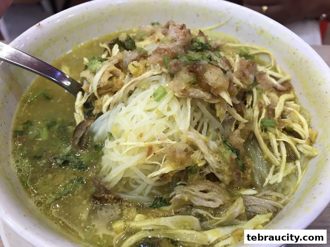 A close-up shot of a delicious bowl of Soto Ayam with shredded chicken and noodles.