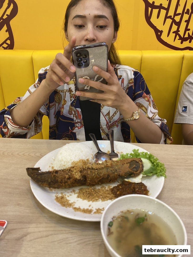 A woman is taking a picture of her fried catfish meal with rice and soup.