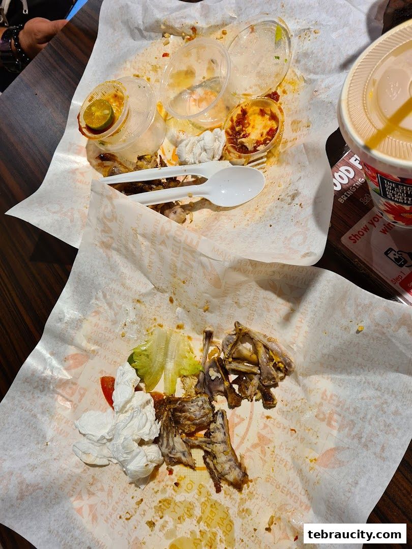A messy table with leftover food scraps, cutlery, and a drink from PenyetPenyet.