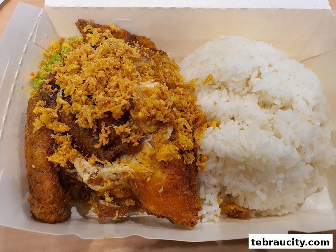 A close-up of a crispy fried chicken dish with rice and crispy toppings in a takeout box.