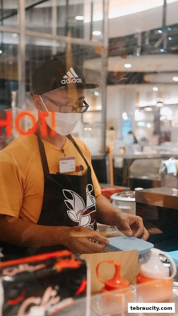 A staff member wearing an apron and mask prepares food behind a counter.