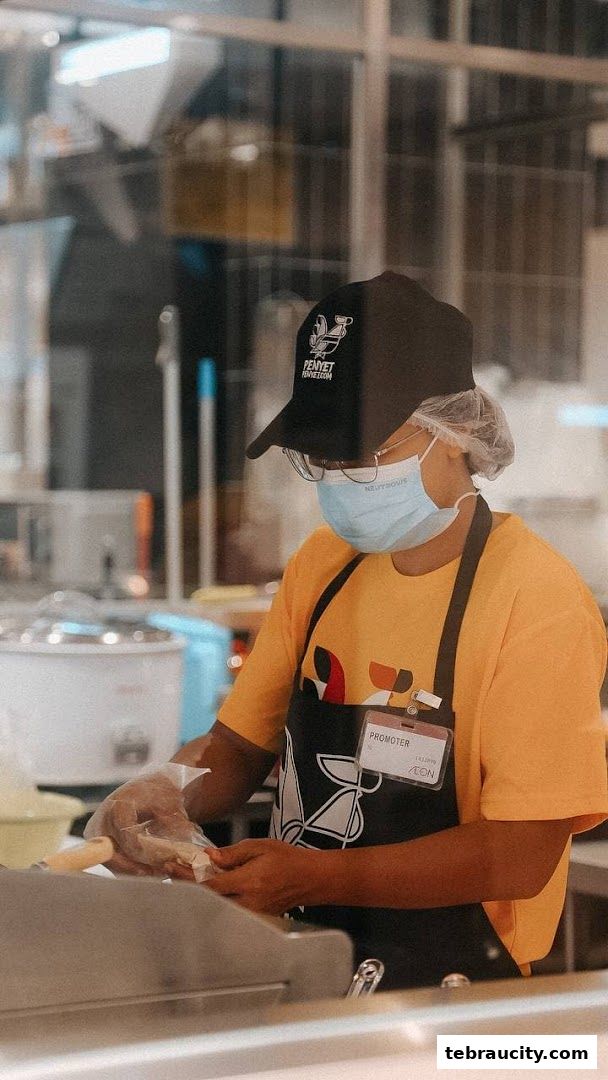 A staff member in a mask and apron prepares food at PenyetPenyet.