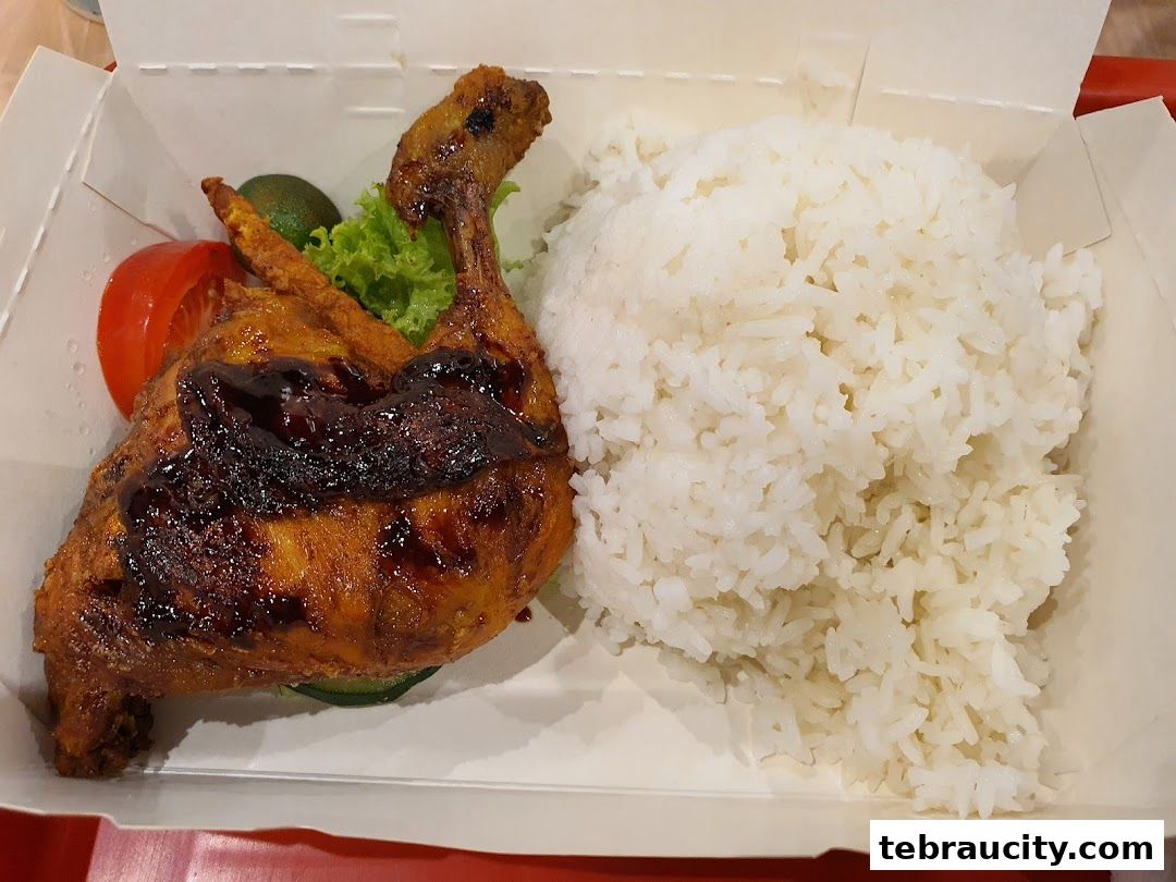 A delicious meal featuring grilled chicken, rice, and fresh vegetables in a takeaway box.