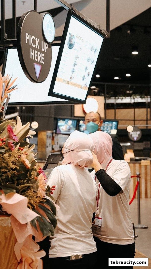 Staff members at a counter with a 'Pick Up Here' sign and a digital menu.