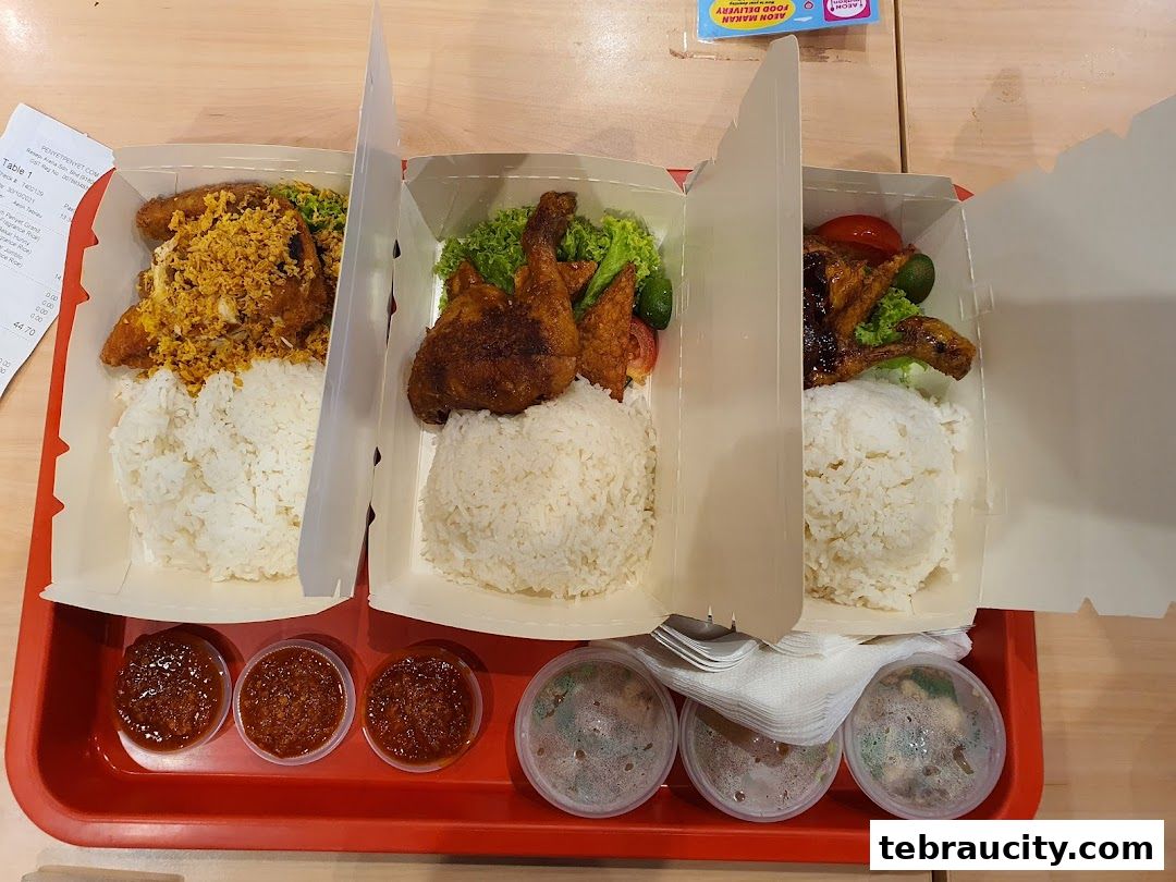 Three takeaway boxes of fried chicken meals with rice and dipping sauces on a red tray.