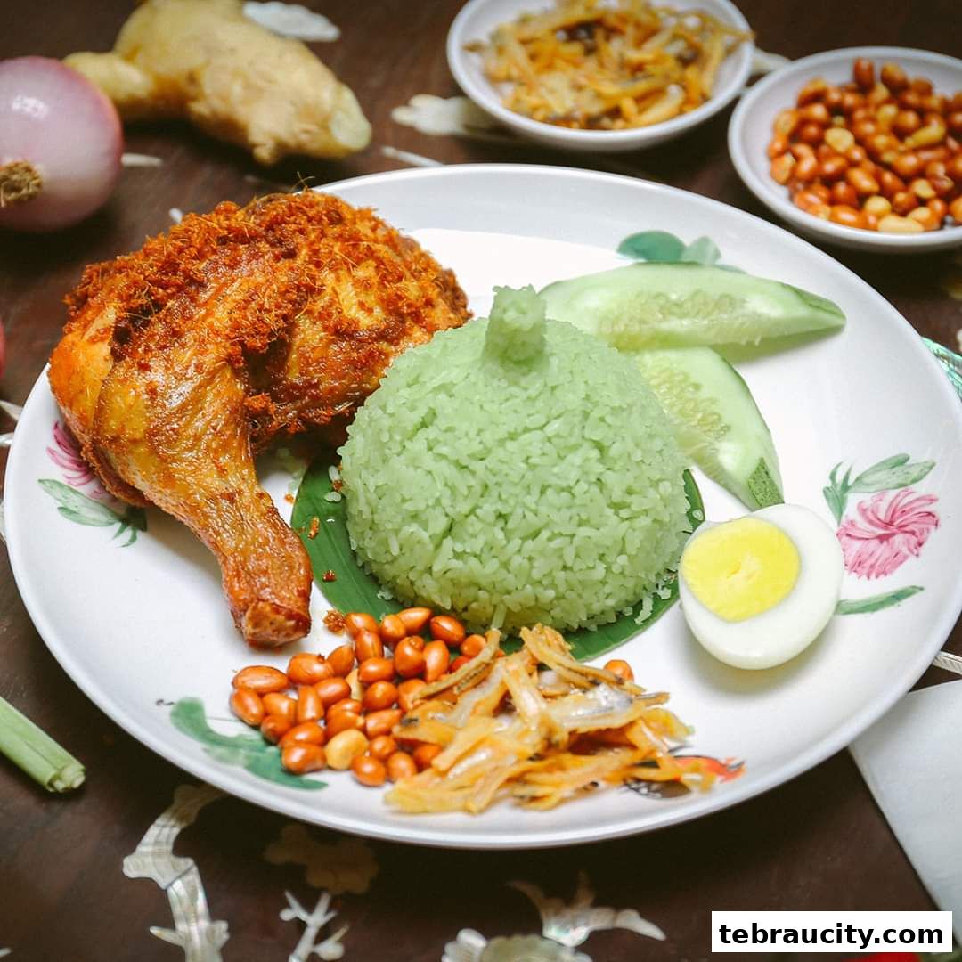 A plate of Nasi Lemak with fried chicken, green rice, egg, and anchovies.