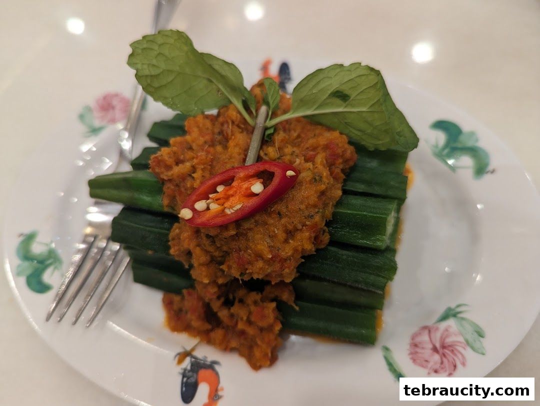 A plate of okra with a spicy topping and chili garnish, served with a fork.
