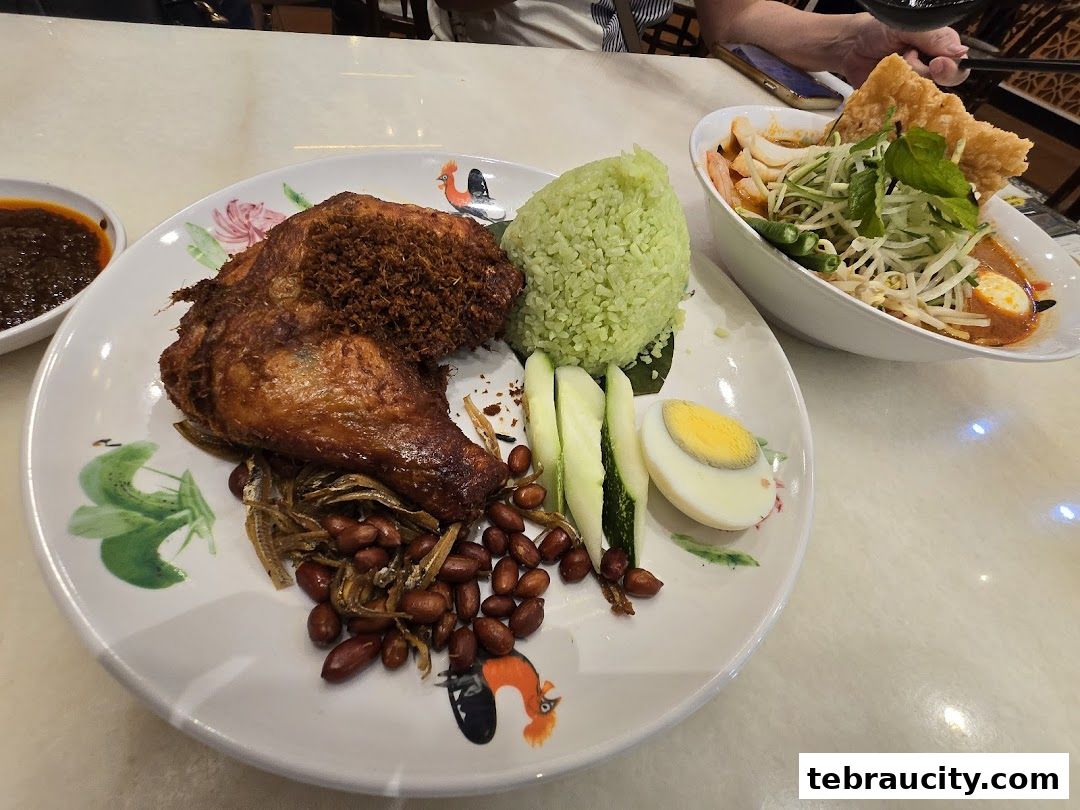 A plate of Nasi Lemak with fried chicken and a bowl of Laksa are displayed on a table.