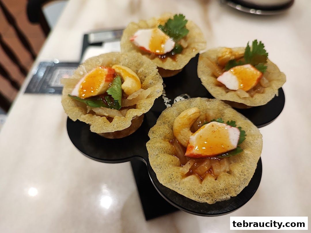 Four crispy appetizers filled with seafood, cashew, and sauce, presented on a black stand.