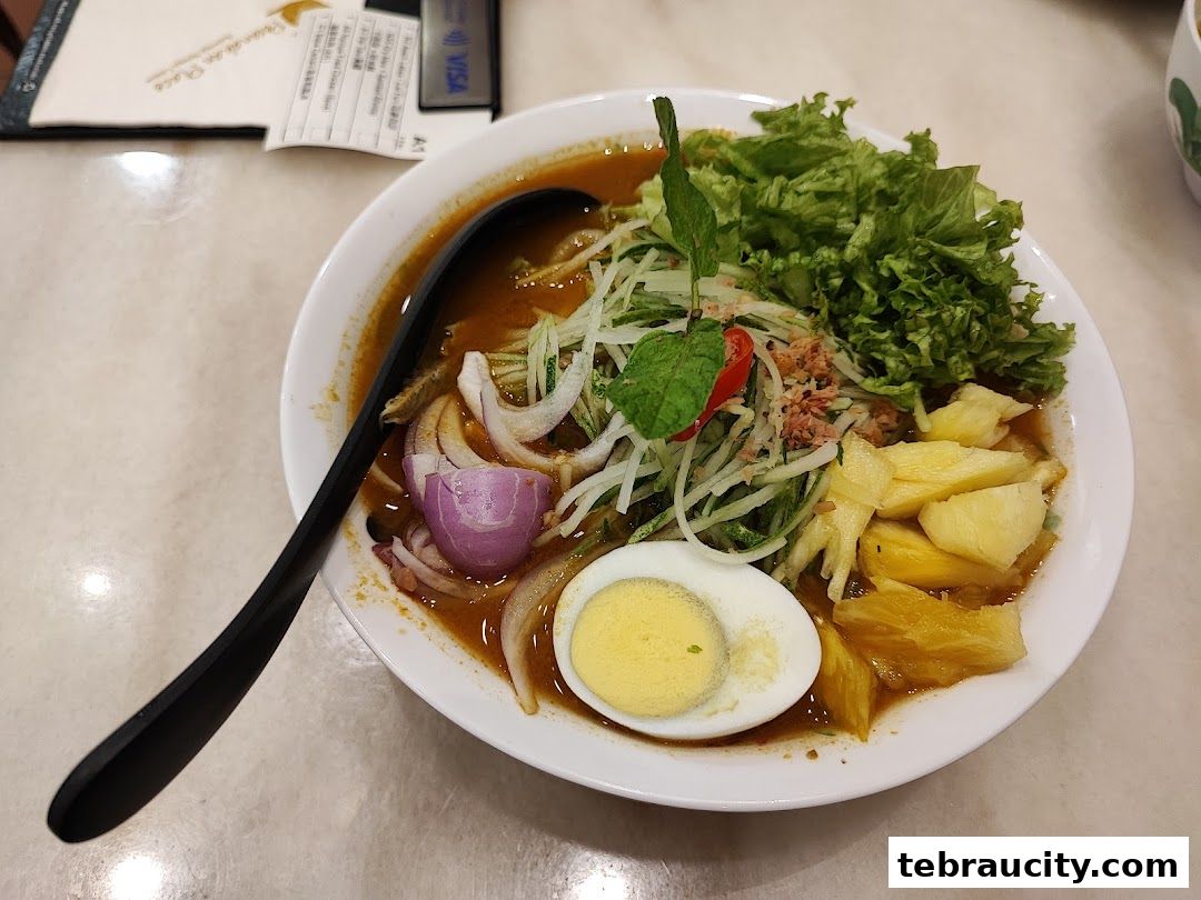 A bowl of delicious Laksa with a boiled egg, pineapple, and fresh vegetables.