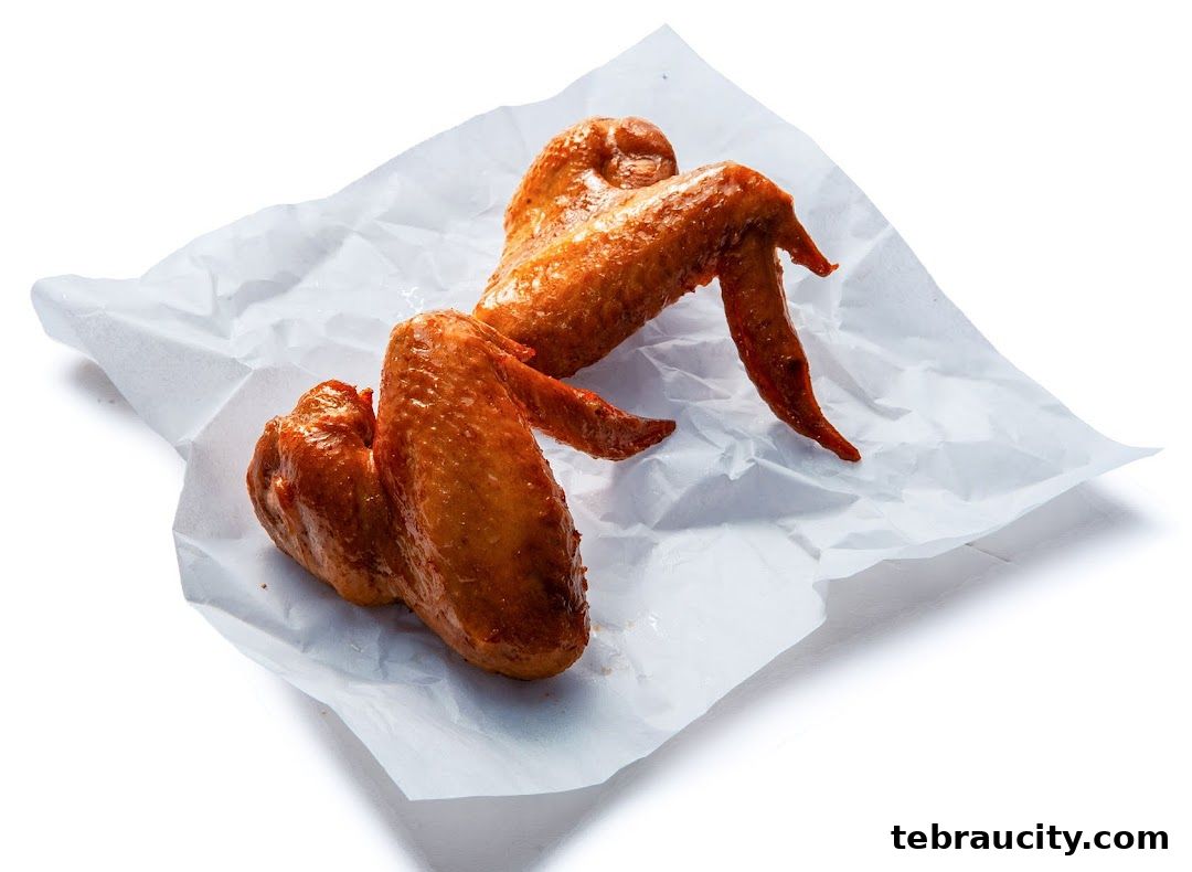 Two delicious, golden-brown chicken wings are presented on crumpled white paper.