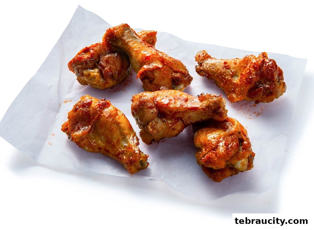 A close-up shot of several delicious, glazed chicken wings arranged on white parchment paper.