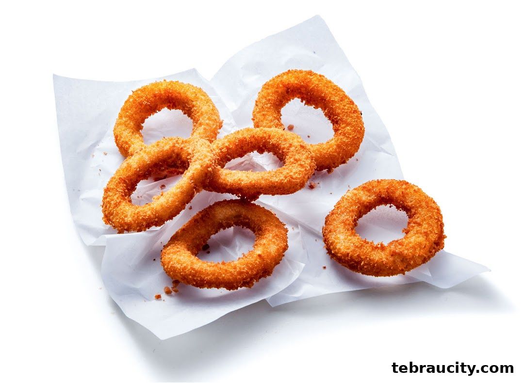 A pile of crispy, golden-brown onion rings served on white paper.