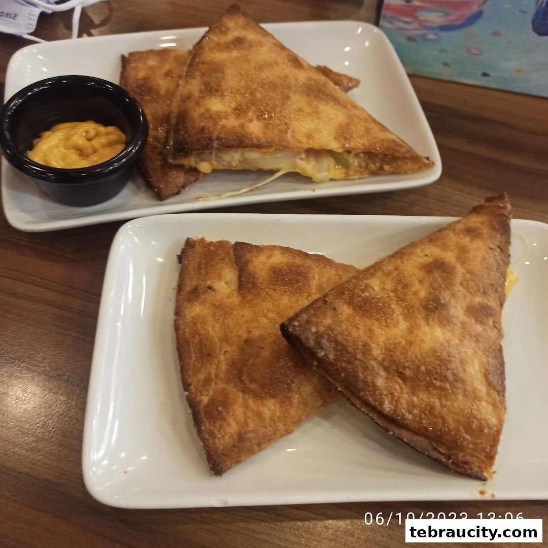 Two plates of triangular-cut quesadillas served with a side of dipping sauce.